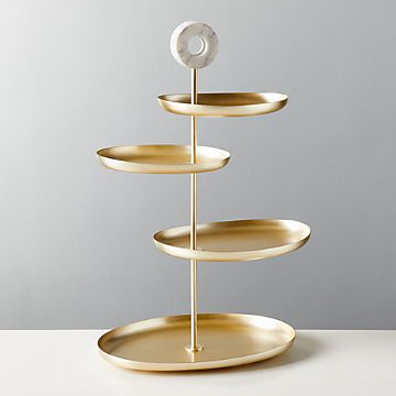 three tiered gold plate stand with white plates on each side and a circular metal object in the middle