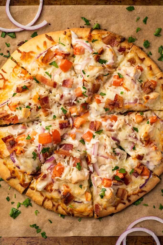 a pizza sitting on top of a wooden cutting board next to onions and carrots