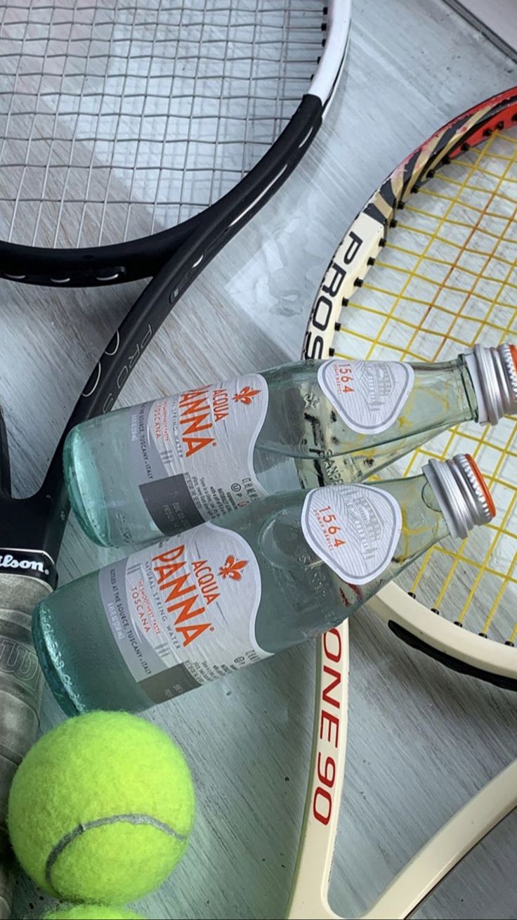 a tennis racket, bottle of gin and two balls on a glass table top