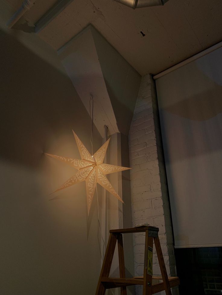 a wooden stool sitting in front of a white wall with a star light on it