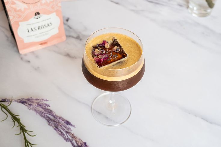 a dessert in a wine glass next to a box of chocolate and lavenders on a marble table