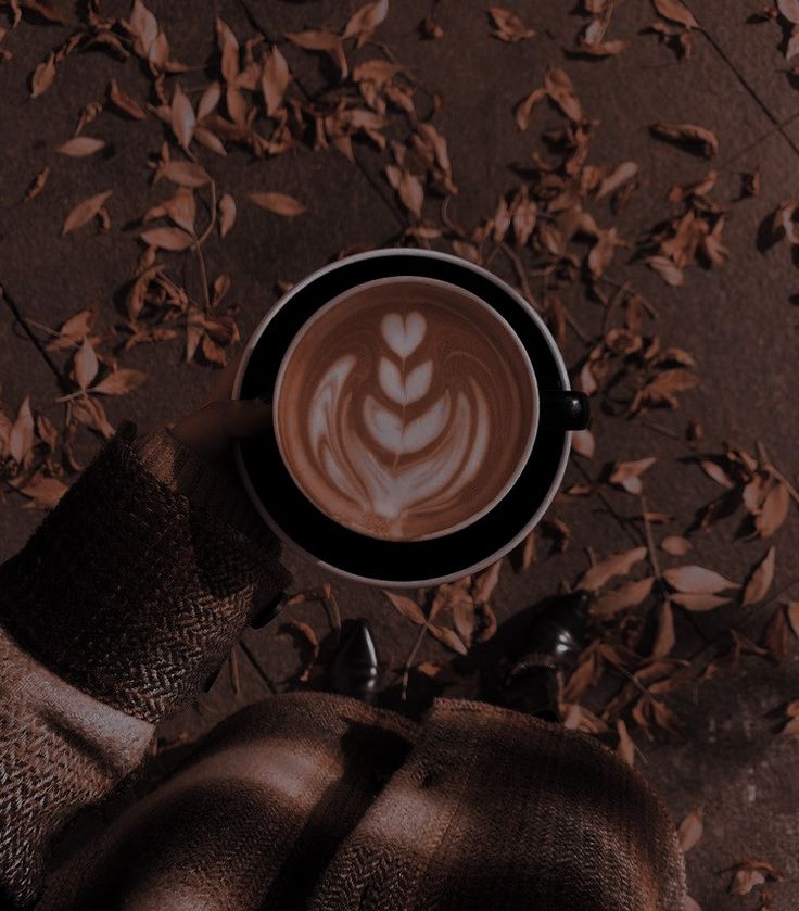 a cappuccino in a black cup on top of a table with leaves around it