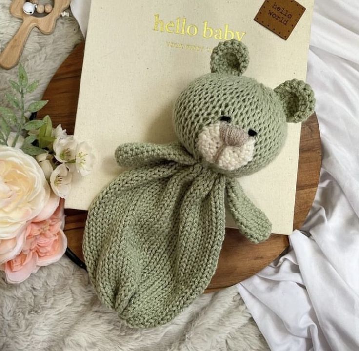 a knitted teddy bear sitting on top of a bed next to an open book