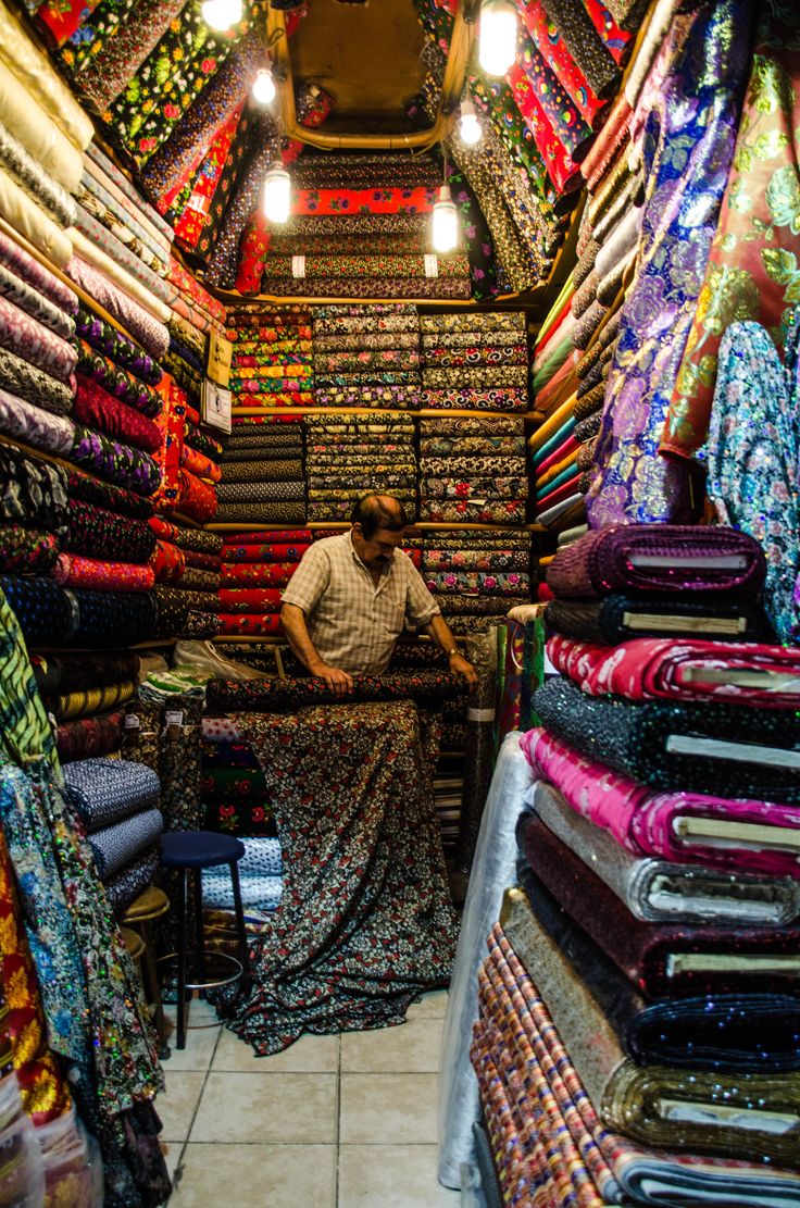 a man sitting in the middle of a store filled with fabrics