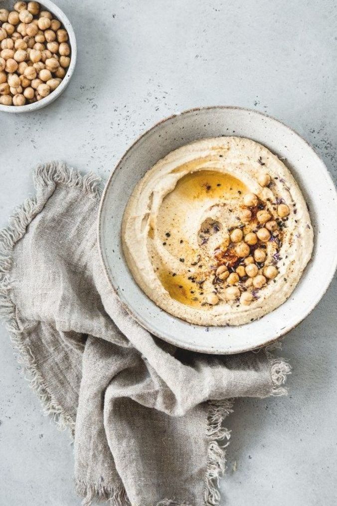 hummus with chickpeas in a bowl on a gray surface next to a cloth