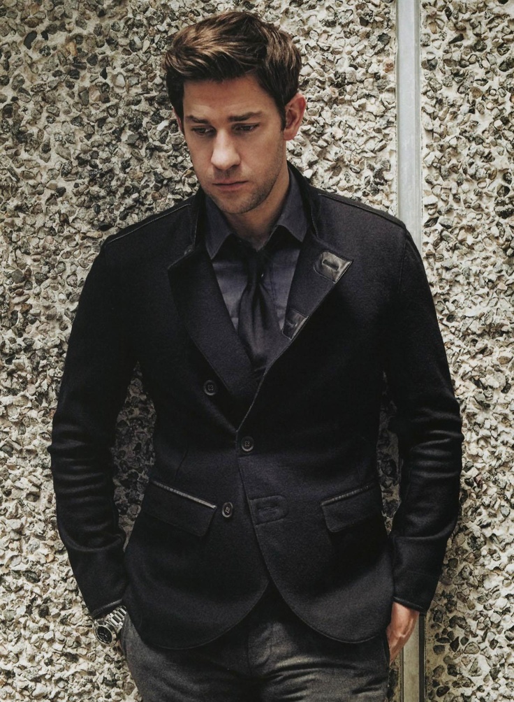 a man wearing a suit and tie standing in front of a wall with pebbles on it