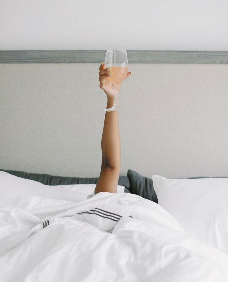 a person laying in bed with their arm up holding a wine glass above their head