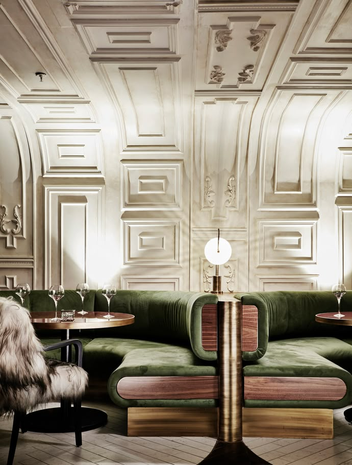 a green couch sitting next to two tables in a room with columns on the wall