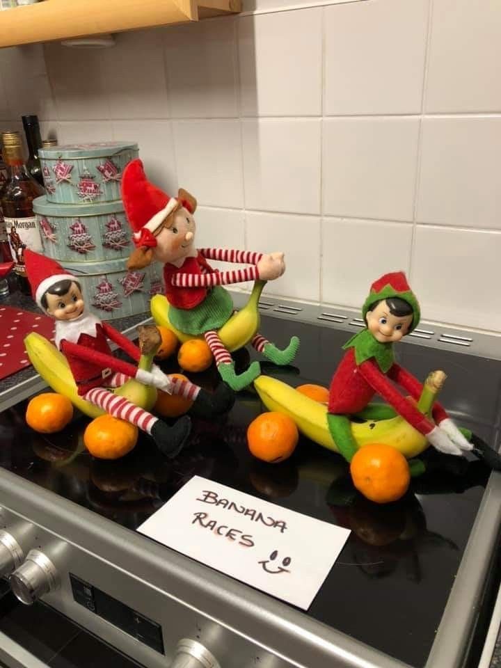 three elf figurines sitting on top of an oven with oranges and bananas