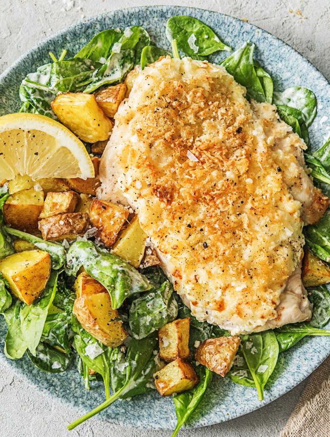 a blue plate topped with chicken, potatoes and spinach on top of a bed of lettuce