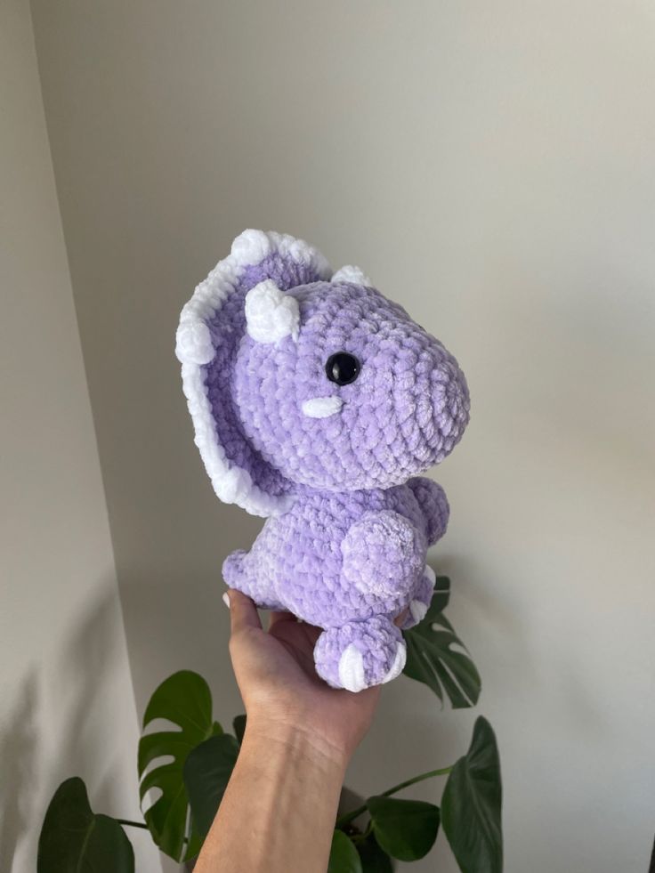 a hand holding up a small crocheted purple elephant with white tusks