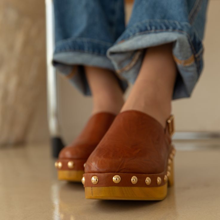 Our Warehouse peanut slingback clogs hit different. The studded detail define this unique silhouette. Wild veg leather upper in cognac Insole: Microsuede Lining material: Linen Outsole: Rubber tread and wood Style type: Slingback clog Heel material: Wood medium shine Platform height: 2.36 inches Gold functional buckle Gold stud embellishment Round toe Hit Different, Clog Heels, Gold Studs, Cognac, Clogs, Buffalo, Peanut, Leather Upper, Buckle