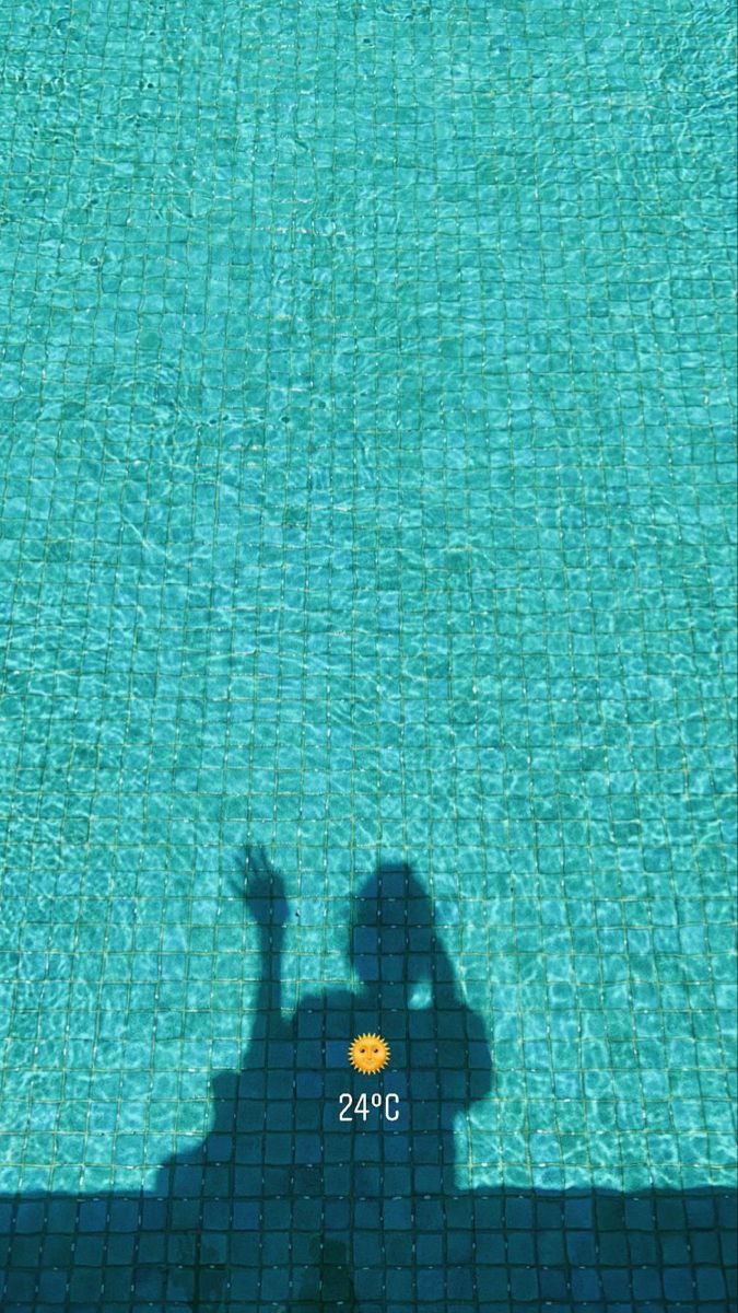 the shadow of a person standing in front of a swimming pool with an orange frisbee