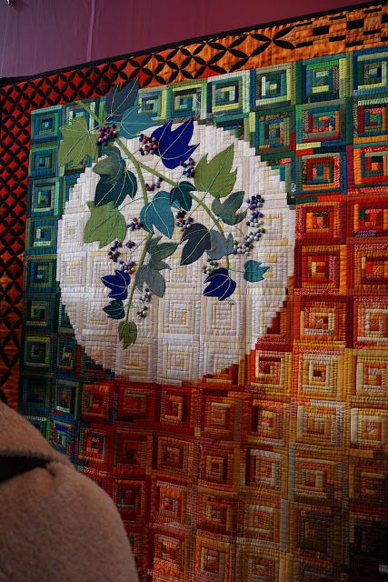 a close up of a quilt with flowers and leaves on the center, in front of a red wall