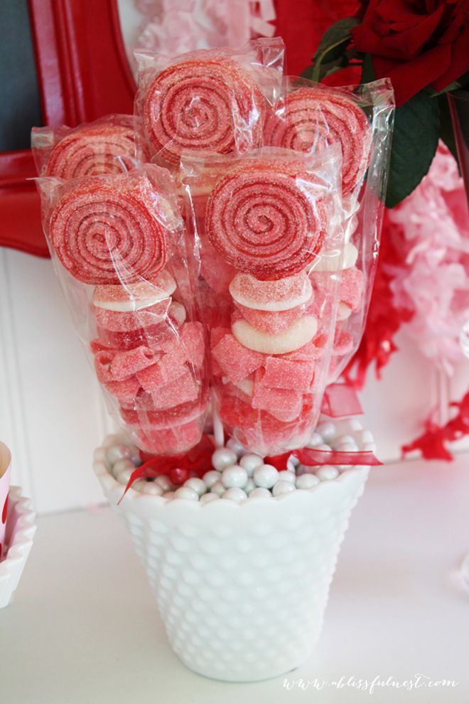 there are many candies in the vase on the table with red roses behind them