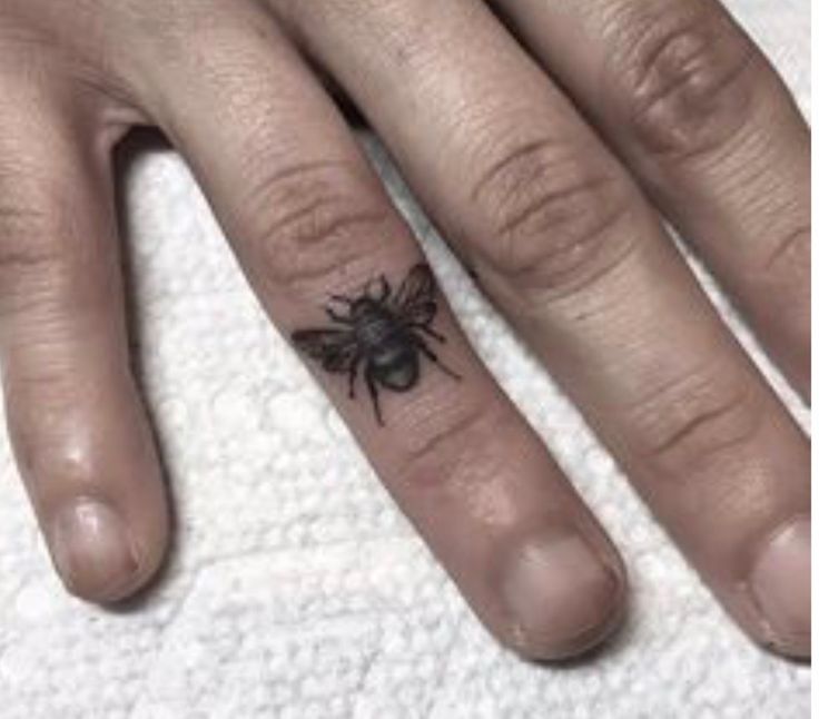 a woman's hand with a small black spider tattoo on her left thumb and finger