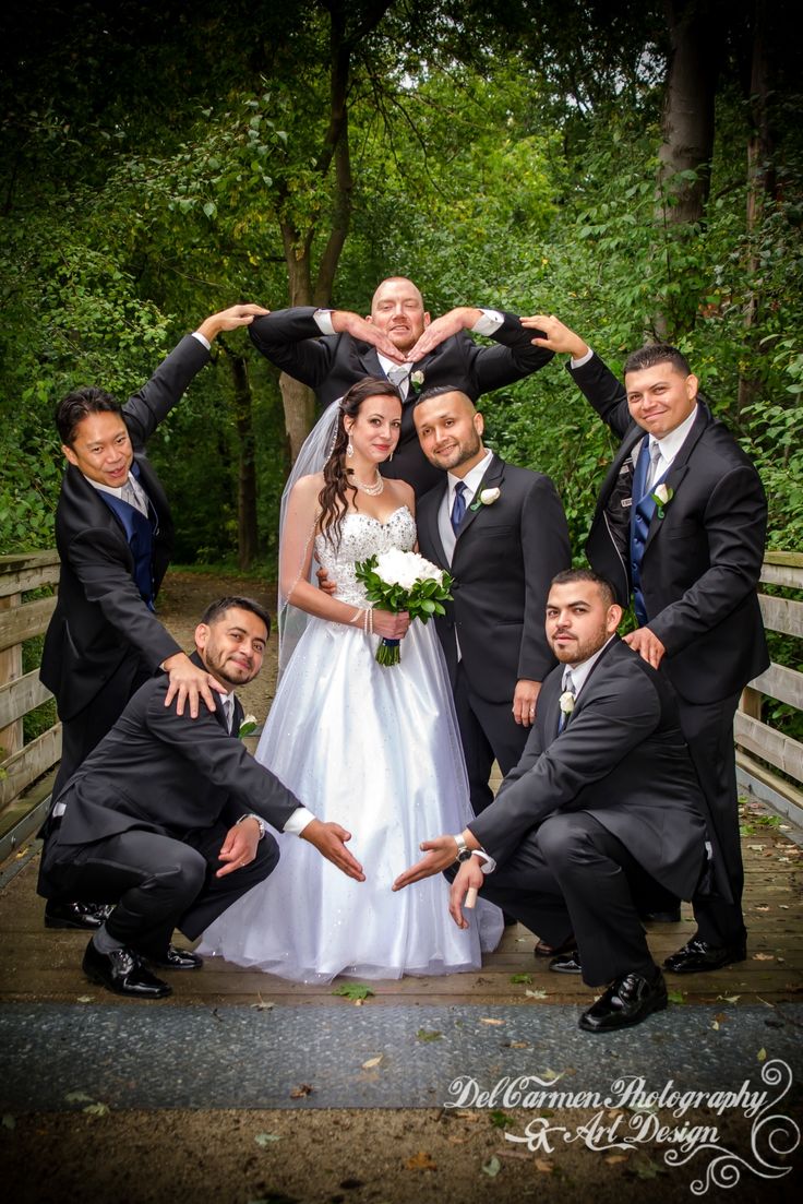 a bride and groom with their wedding party posing for a photo on a bridge in the woods