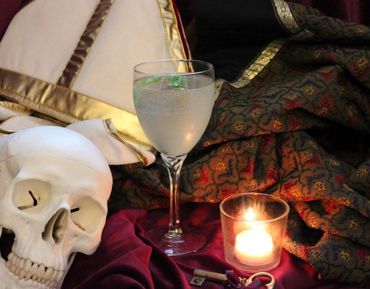 a candle and a skull sitting on a bed next to a glass with liquid in it