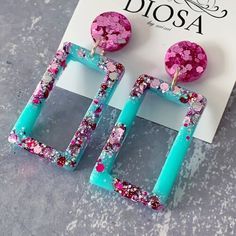 the pink and blue square earrings are on display next to a sign that says diosa