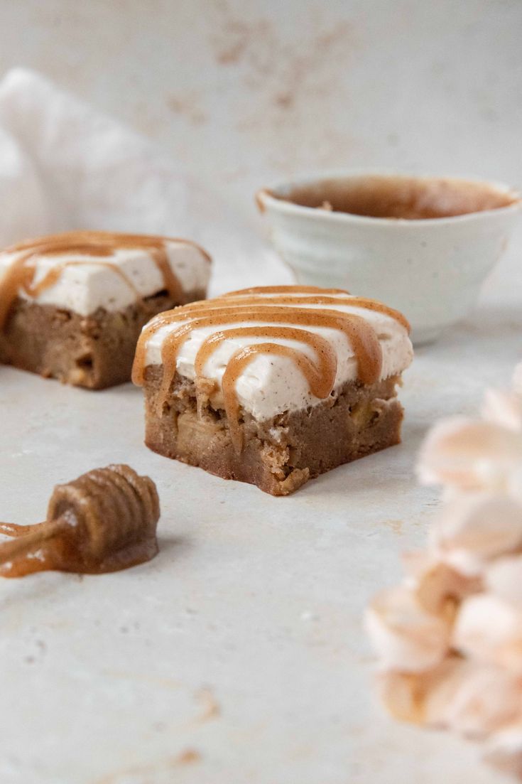 three pieces of dessert with caramel drizzled on them and some flowers in the background