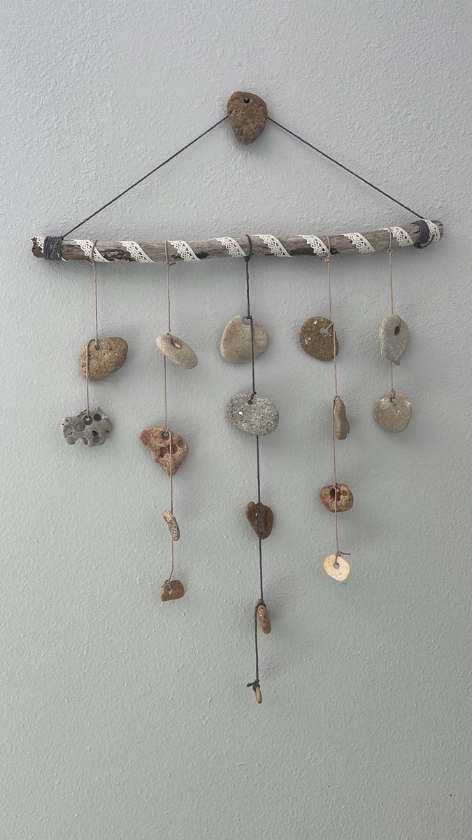 a wind chime hanging from the side of a wall with rocks and shells on it