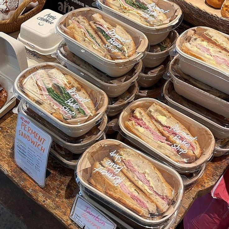 several trays of sandwiches on display at a bakery counter with pastries in the background