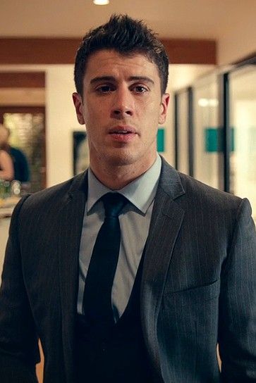 a man wearing a suit and tie standing in an office hallway looking at the camera