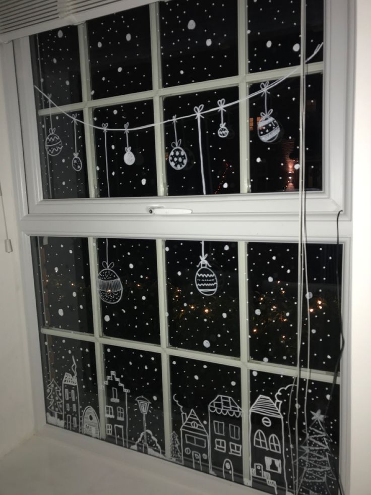 a window with christmas decorations drawn on the glass and string lights hanging from it's sides