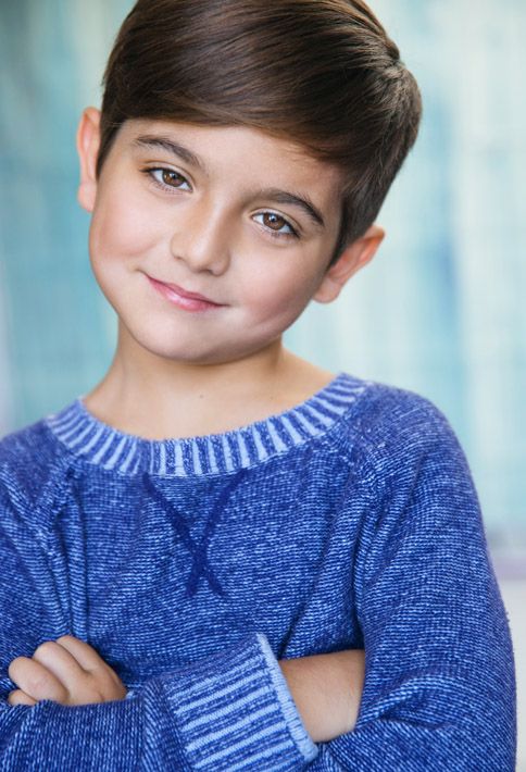 a young boy wearing a blue sweater posing for a photo with his arms crossed in front of him