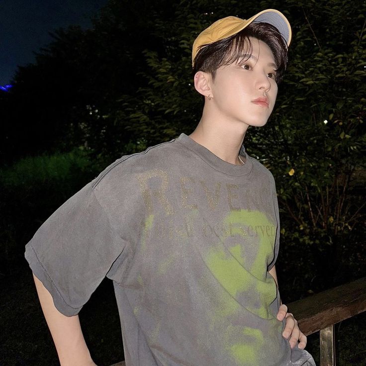 a young man standing next to a wooden bench at night wearing a hat and t - shirt