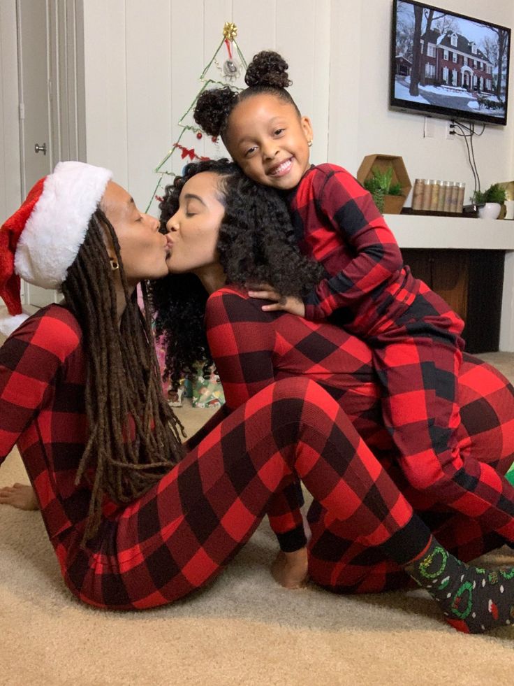 two women in matching pajamas are kissing each other while sitting on the floor next to a christmas tree