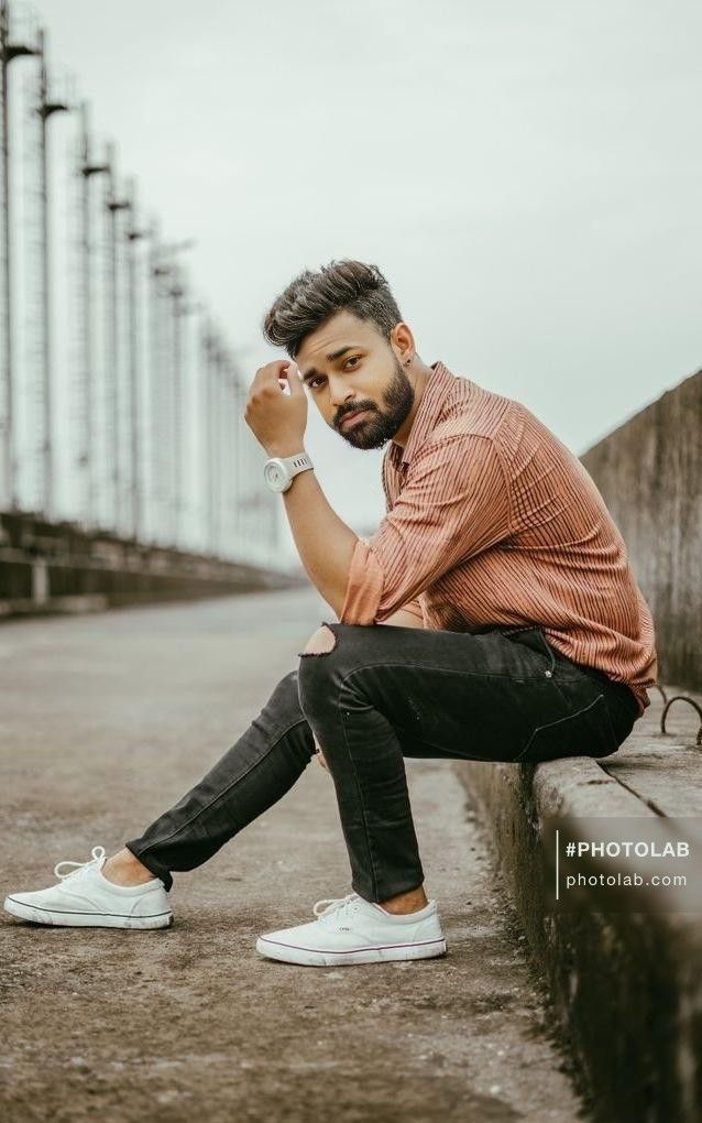 a man with a beard sitting on a wall and looking at the camera while holding his hand to his face