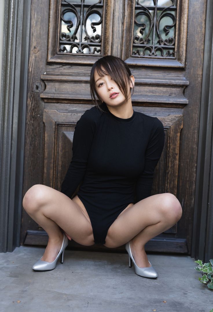 a woman sitting on the ground in front of a door with her legs crossed and wearing high heels