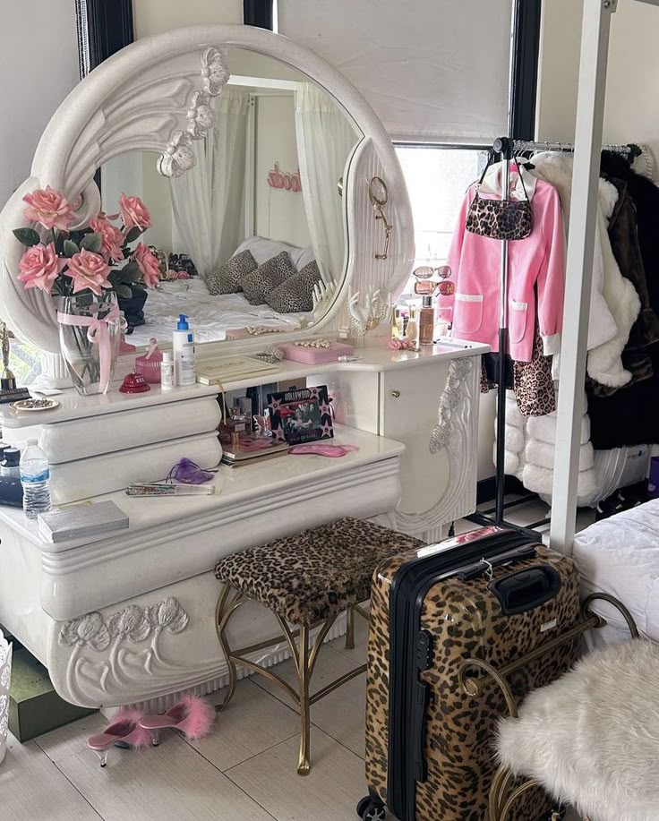 a dressing table with a mirror, leopard print stool and pink flowers on it in front of a window