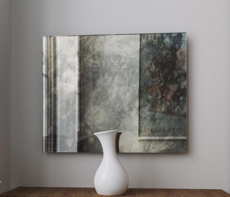 a white vase sitting on top of a wooden table in front of a framed painting