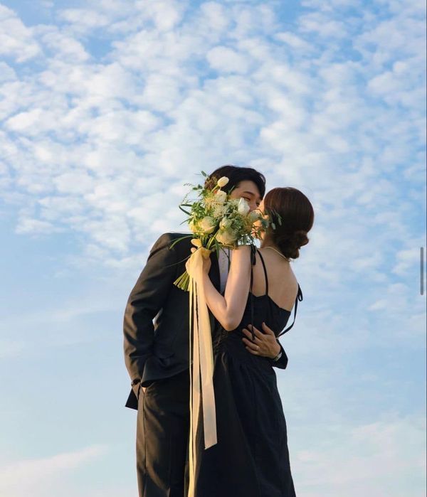 a man and woman standing next to each other under a blue sky with white clouds