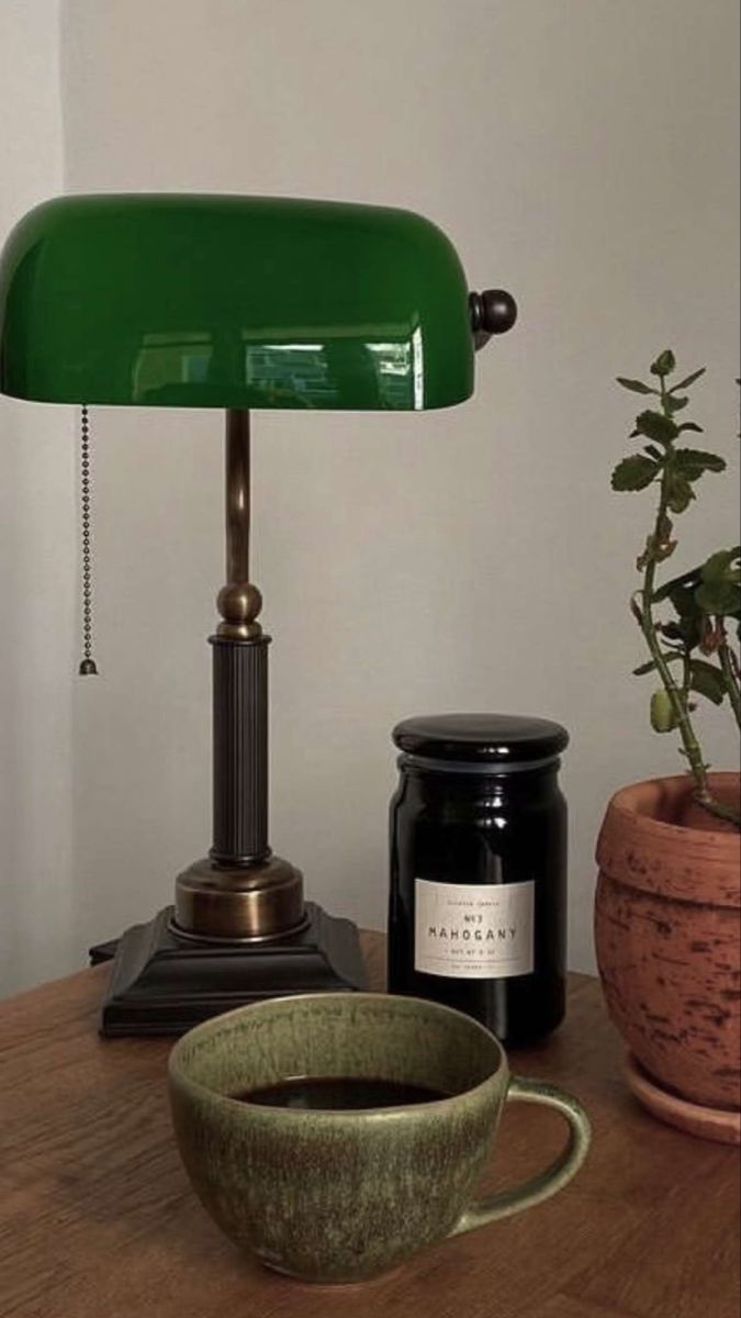 a green lamp sitting on top of a wooden table next to a cup of coffee