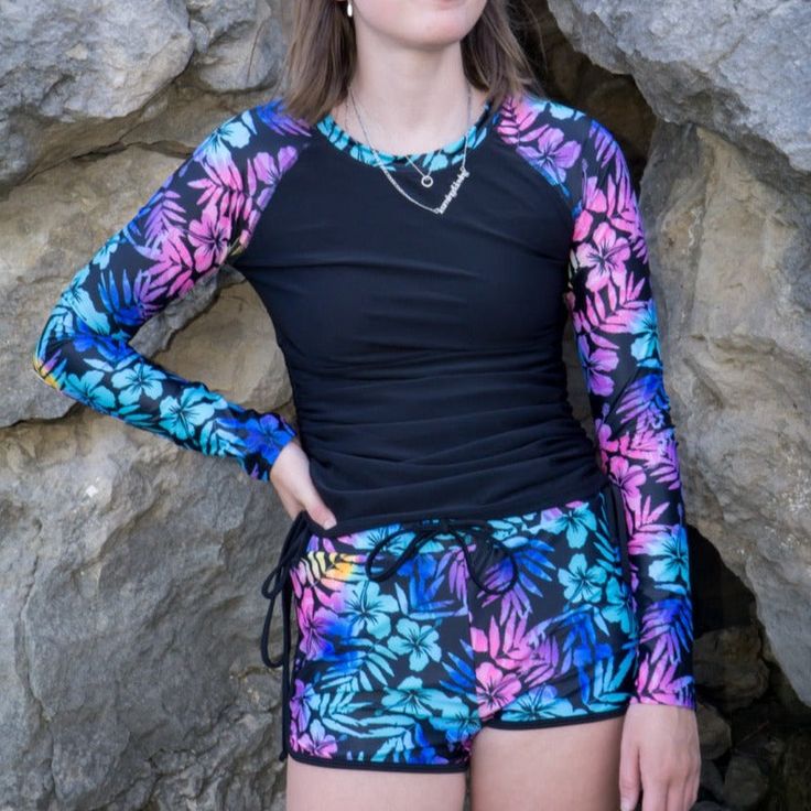 Women's Boyshort Rashguard Swimsuit Set-Black Ombre Hawaiian Floral This 2 pc swimsuit set offers UPF 40 Long Sleeve Rash Guard and Dolphin Hem Swim Shorts. Women's UPF long-sleeve rash guard and swim shorts set - This swimsuit provides superior sun protection and is lined for additional comfort. The rashguard is adjustable with its side ties, allowing you to alter the length for a perfect fit. The shorts also feature an inner lining, mid-rise waist, and full bum coverage for a sporty, comfortab Tropical Swimwear With Built-in Shorts For Poolside, Tropical Swimwear With Built-in Shorts, Tropical Swimwear With Built-in Shorts For Beach Season, Beachwear Stretch Rash Guard For Vacation, Fitted Tropical Swim Trunks For Pool, Tropical Swimwear With Built-in Shorts For Beach Party, Multicolor Beachwear Rash Guard For Pool, Beach Party Swimwear With Built-in Shorts, Black Tropical Swimwear For Poolside