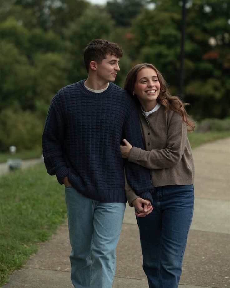 a young man and woman walking down a sidewalk holding each other's hands as they smile