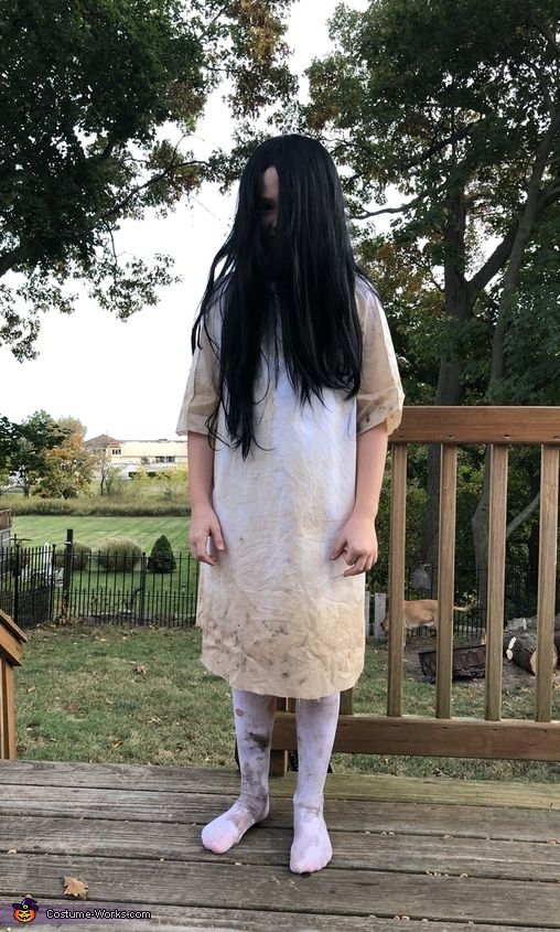 a woman with long black hair standing on a deck wearing a white dress and tights