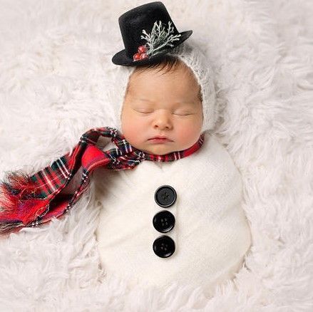 a newborn baby wearing a snowman hat and scarf is sleeping on a white blanket