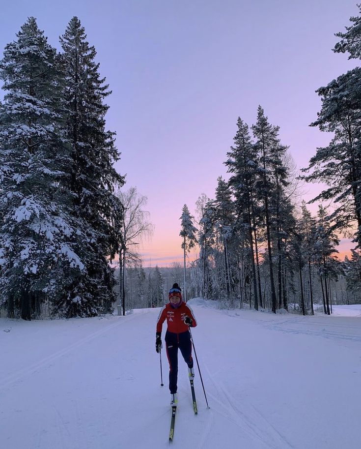 a man riding skis down a snow covered slope next to tall pine tree's