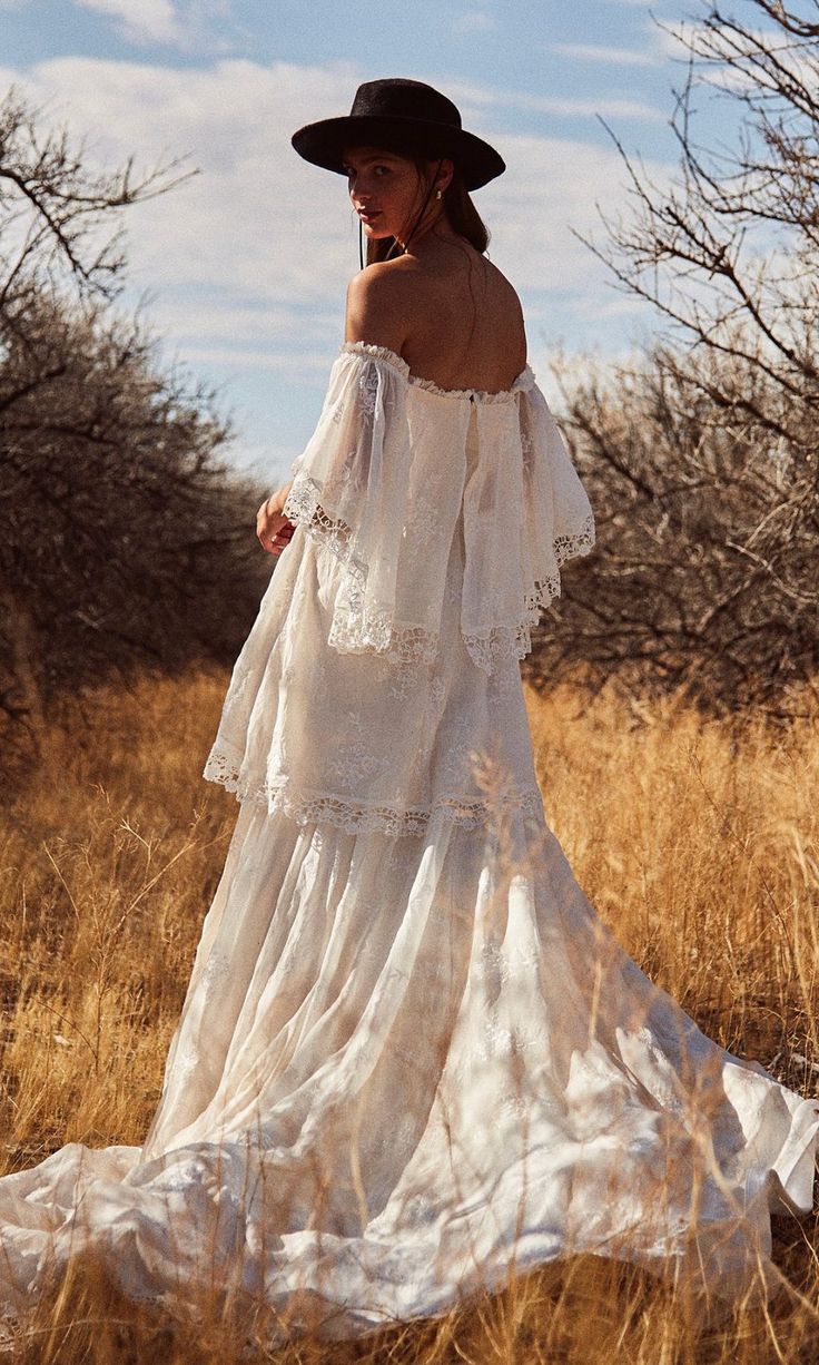 a woman in a white dress and black hat is walking through tall grass with her back to the camera