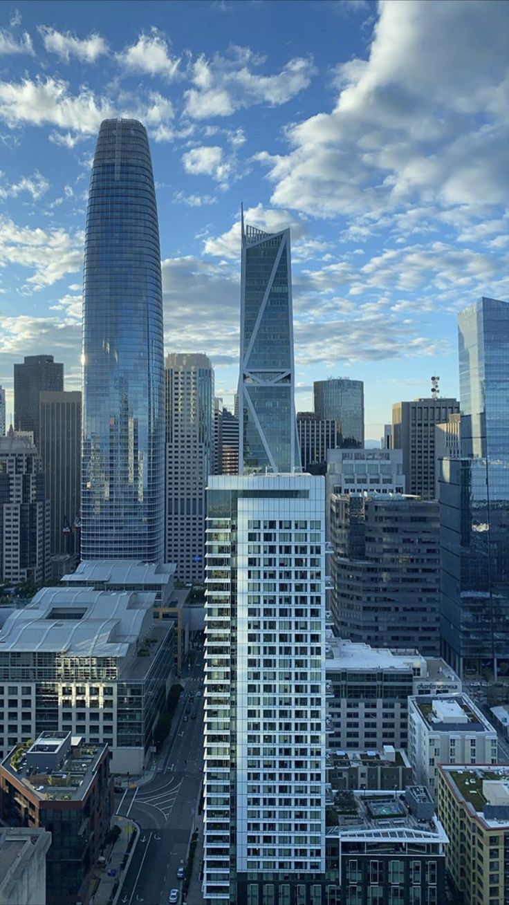 an aerial view of the city with skyscrapers and buildings in the foreground, under a cloudy blue sky