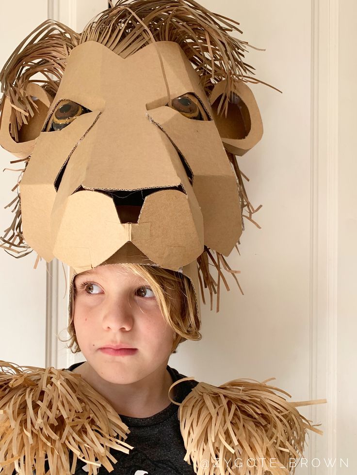 a young boy wearing a lion mask made out of cardboard and paper mache strips