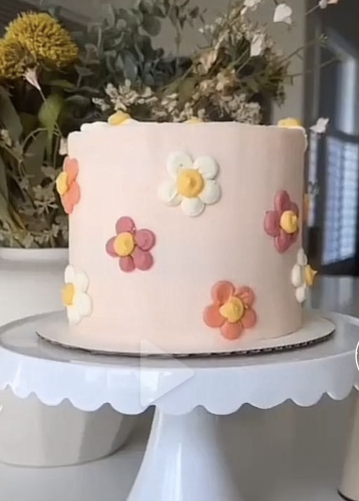 a pink cake with flowers on it sitting on a table next to a potted plant