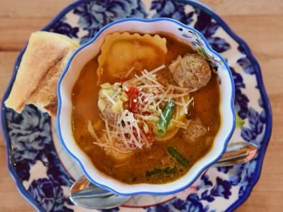 a bowl of soup with meatballs, cheese and bread on a blue and white plate