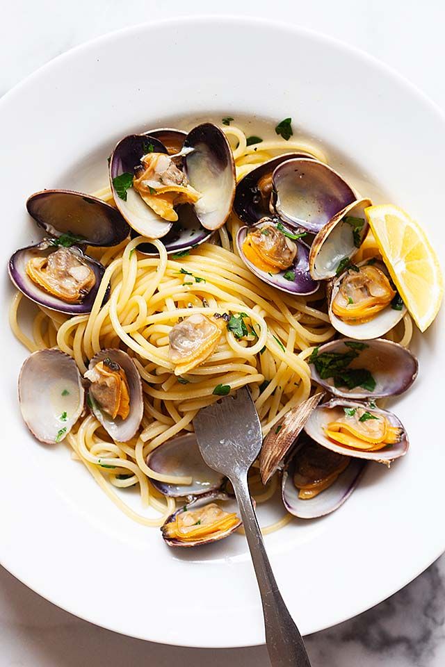 a white bowl filled with pasta and clams on top of a marble countertop