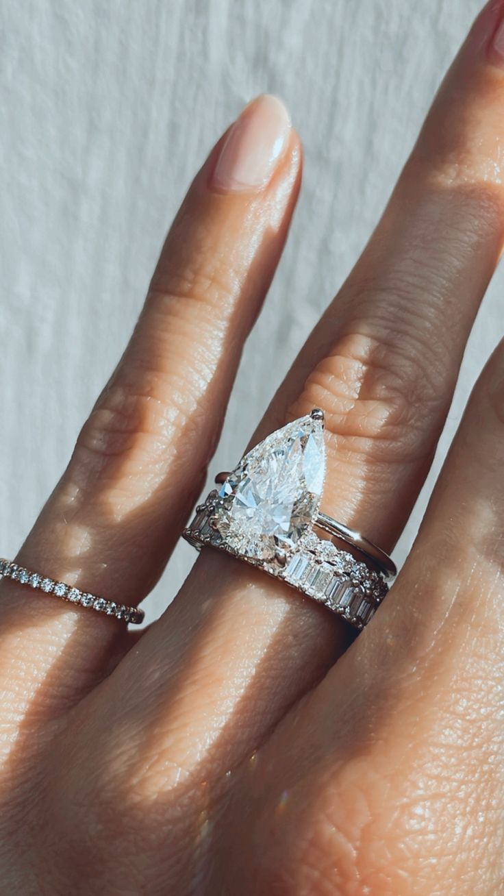 a woman's hand with a diamond ring on top of her finger and an engagement band