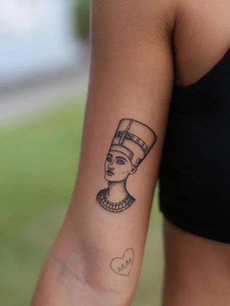 a woman's arm with an egyptian tattoo on her left arm and a heart in the middle